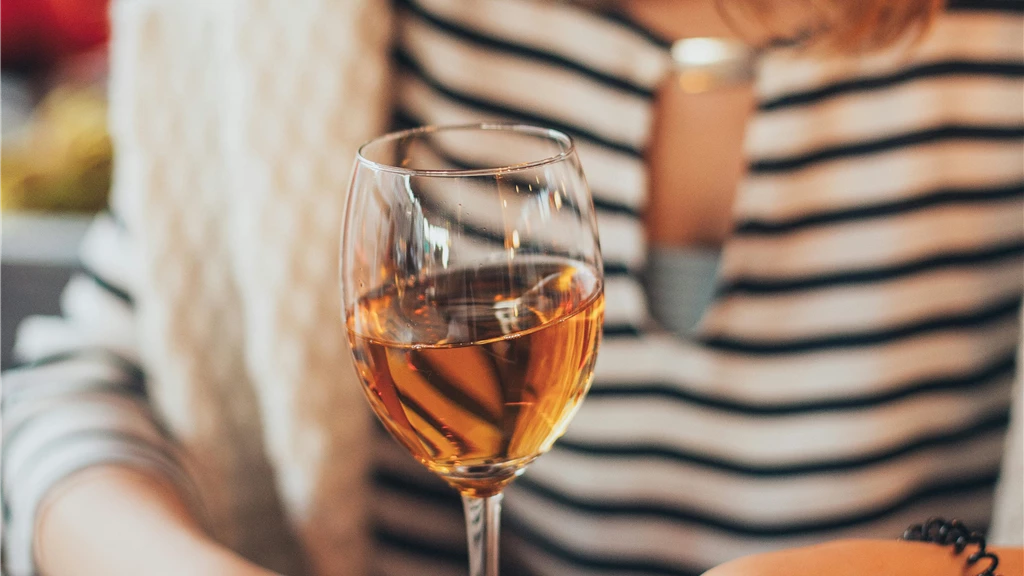 A woman with striped shirt holding a wine glass indoors, creating a warm and fashionable ambiance.