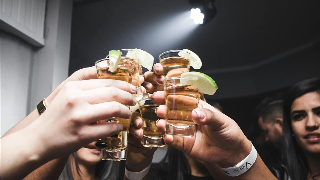 Friends raising tequila shots with lime in a lively indoor bar setting.