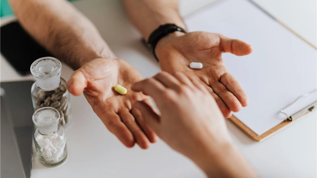 Close-up of hands exchanging pills in a clinical environment.