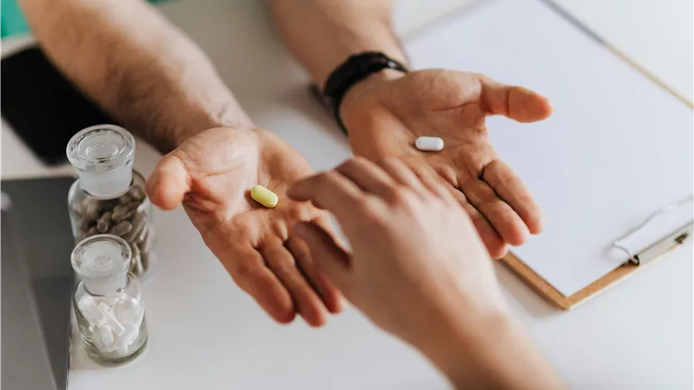 Close-up of hands exchanging pills in a clinical environment.