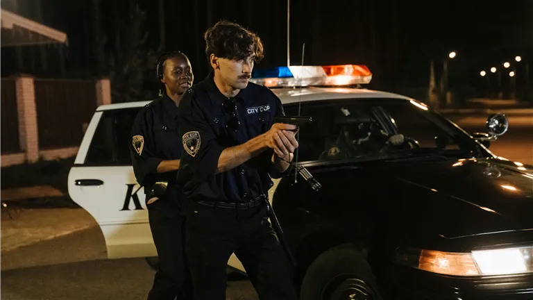 Police officers engaged in nighttime operation with a patrol car on a dimly lit street.