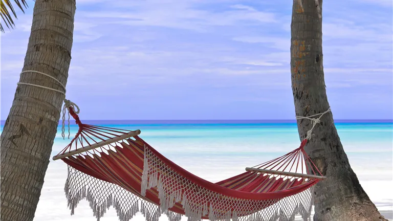 Idyllic beach hammock between coconut trees with azure blue waters.