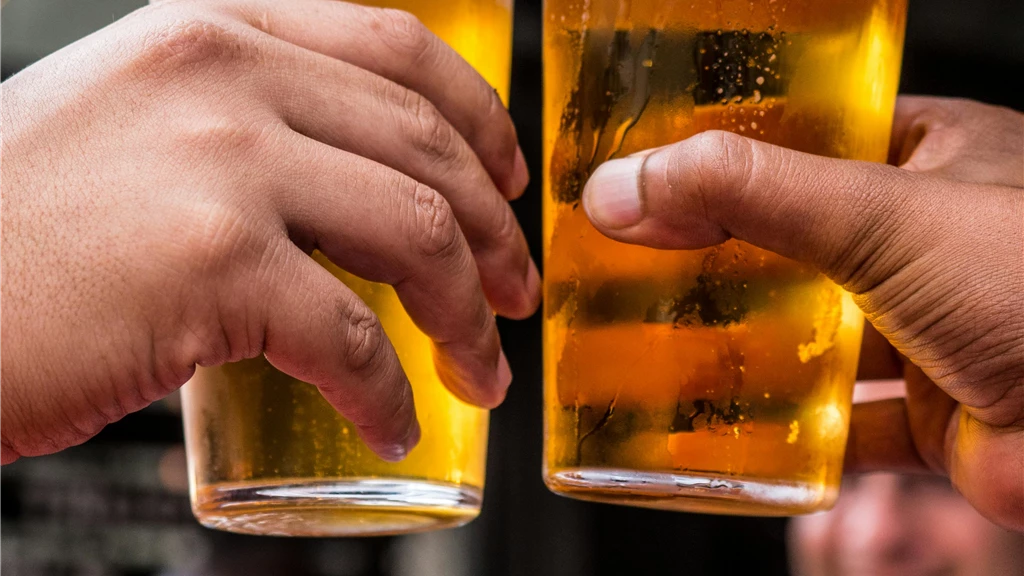 Close-up of two friends toasting with cold beer glasses at a lively bar, celebrating friendship and good times.