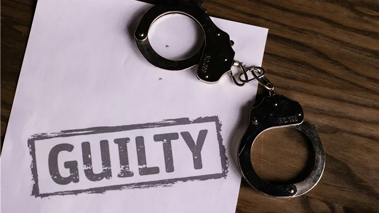 Top view of handcuffs on paper with 'GUILTY' text, symbolizing a verdict or crime.