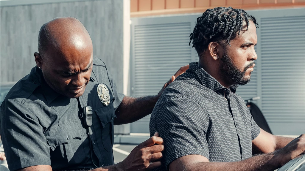 A police officer handcuffs a suspect in a dramatic arrest scene outdoors in daylight.