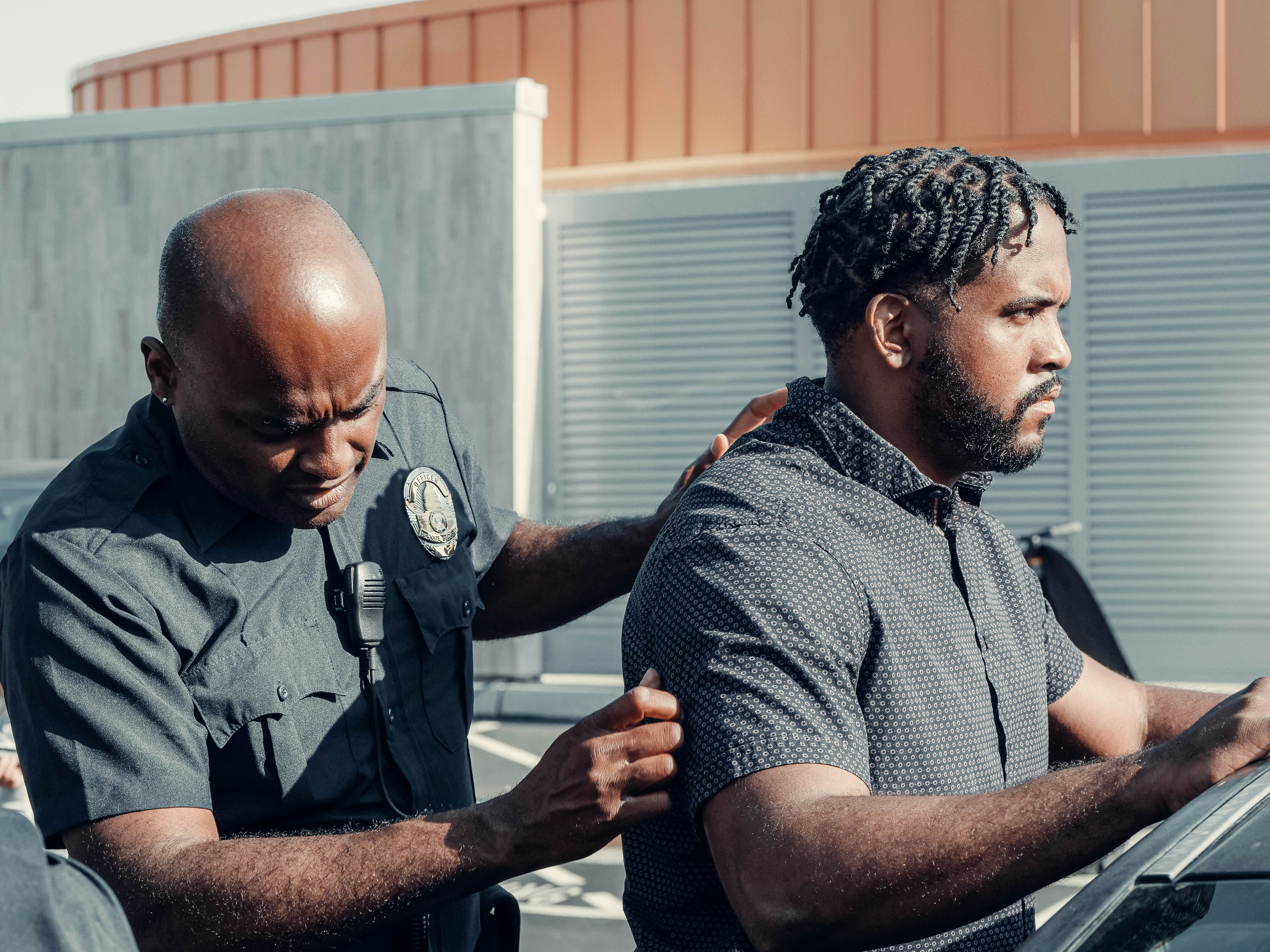 A police officer handcuffs a suspect in a dramatic arrest scene outdoors in daylight.