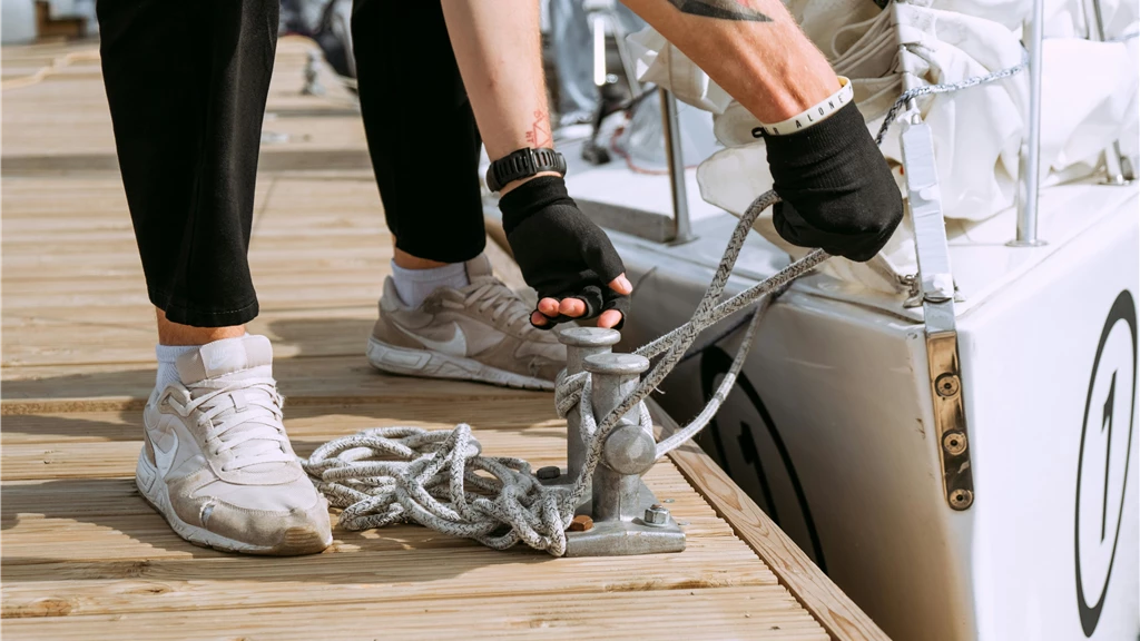 Close-up of a sailor tying a yacht to the dock using mooring rope. Nautical activity outdoors.