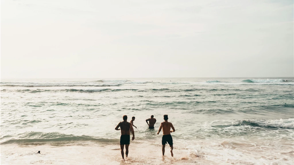 Three friends run into the ocean on a sunny day at a scenic beach in Bali.