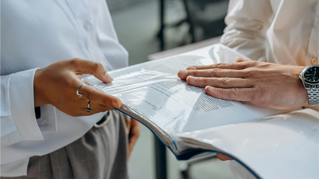 Two professionals examining business documents during a meeting indoors.