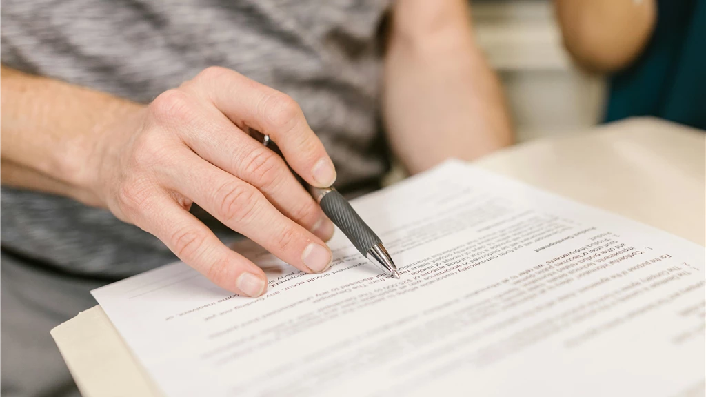 Close-up of a person's hand signing an important legal document with a pen indoors.