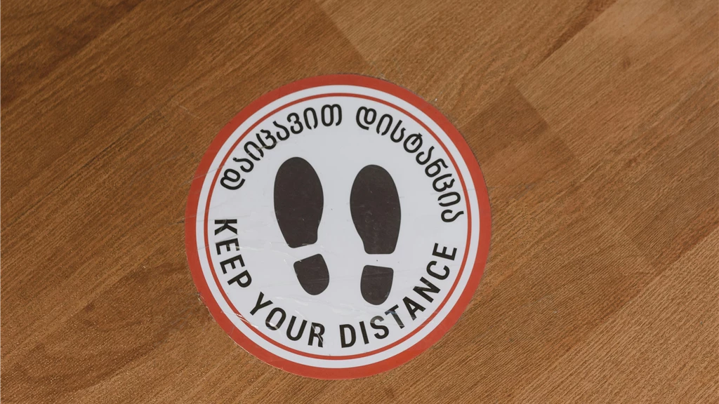 Circular floor sign with 'Keep Your Distance' message on wood floor.