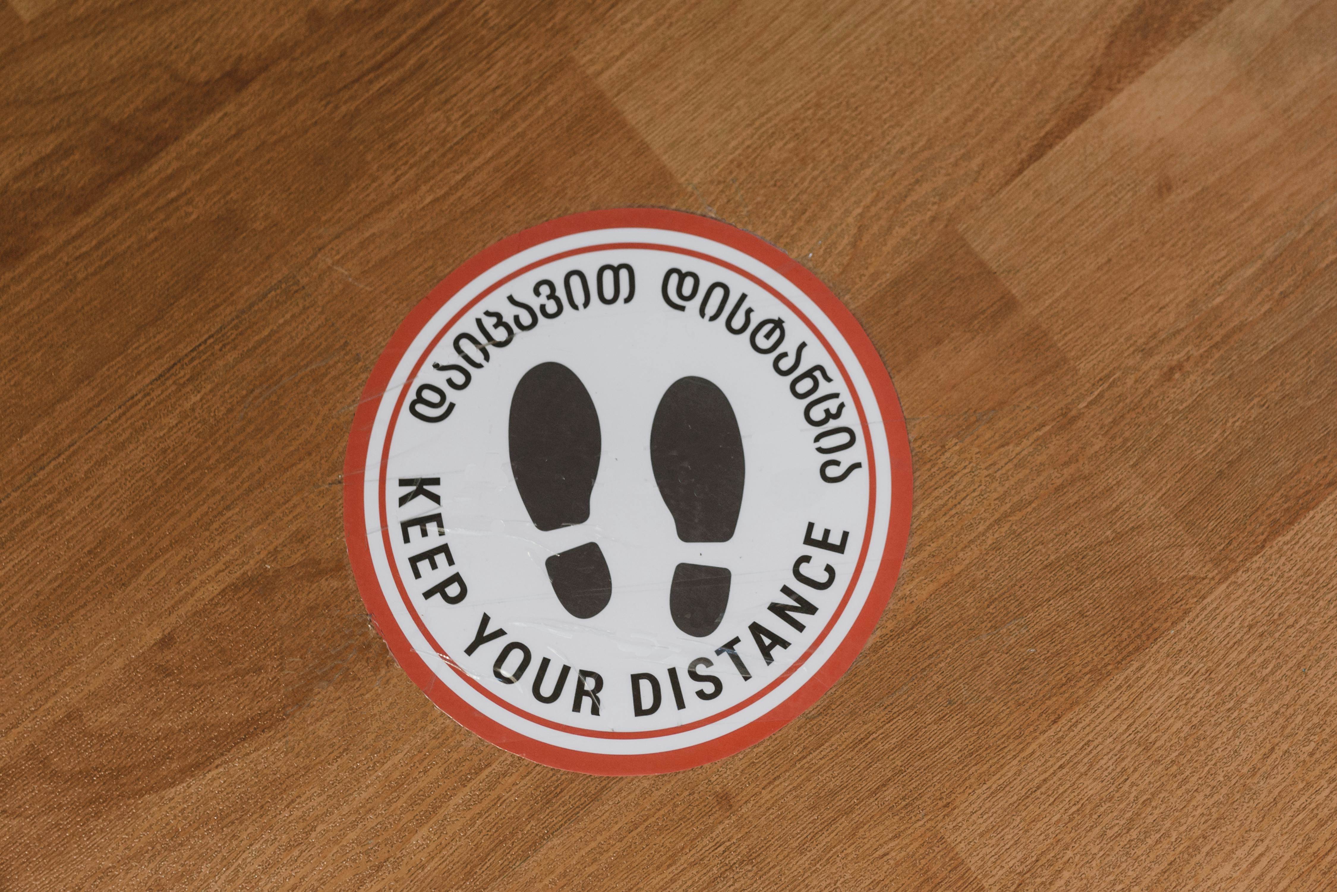 Circular floor sign with 'Keep Your Distance' message on wood floor.