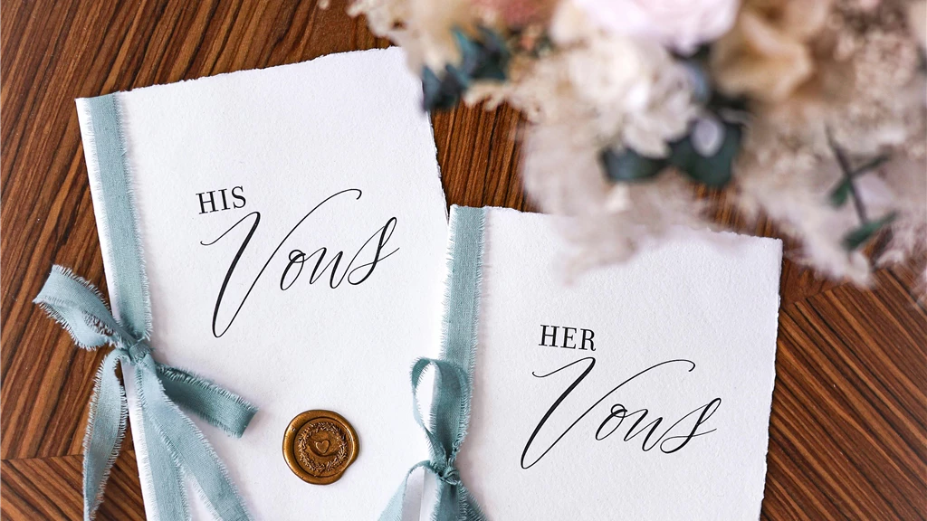 Beautifully styled his and her vow books with a floral bouquet on a wooden table, perfect for weddings.