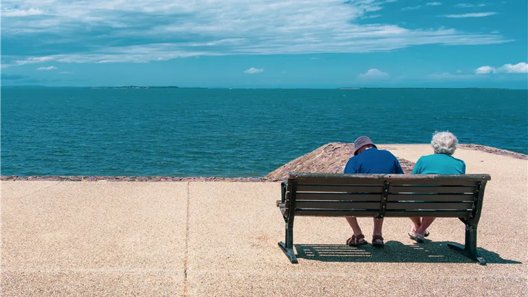 Senior couple relaxing on a seaside bench, enjoying a sunny summer day overlooking the ocean.
