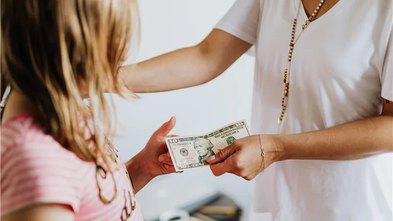 A woman handing money to a young girl, symbolizing family financial education and transactions.