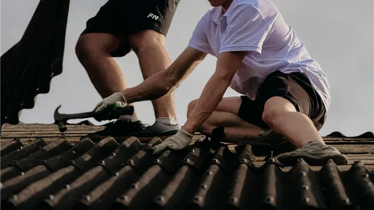 Two construction workers fixing roof tiles, emphasizing teamwork and safety with helmets.