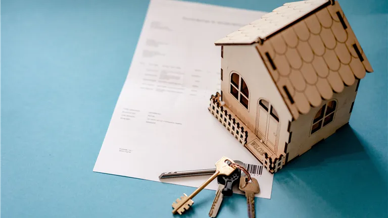 Miniature wooden house with keys and contract symbolizing real estate transactions.