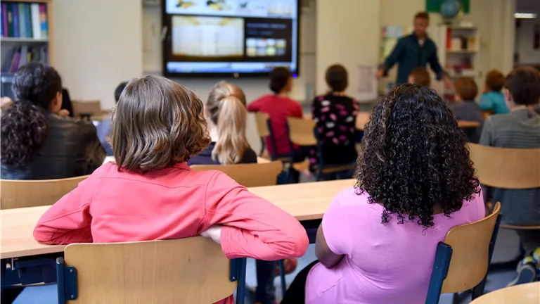 Students attentively watching a lesson on a smart board in a colorful Dutch classroom.