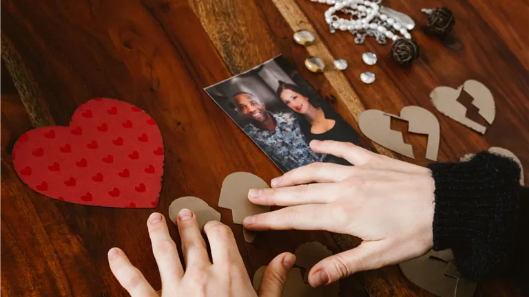 Close-up of hands arranging broken hearts near a couple's photo on a wooden table.